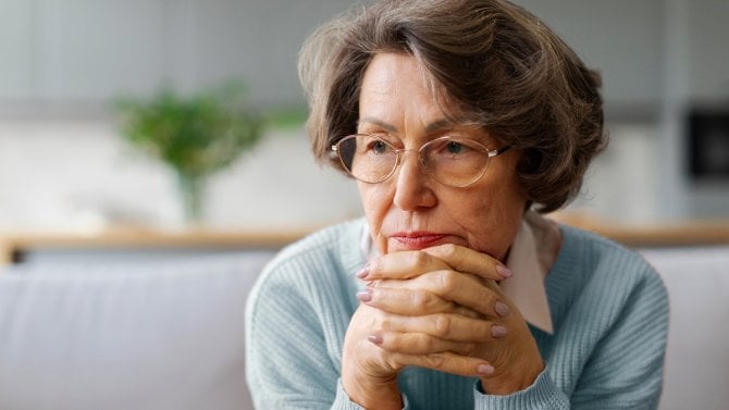 https://www.finance.cz/images/Žena v důchodovém věku v brýlích, sedí, má bradu v rukách a tváří se ustaraně
