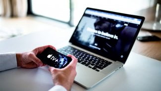 Telefon s logem APPLE TV+, notebook v pozadí obrázku